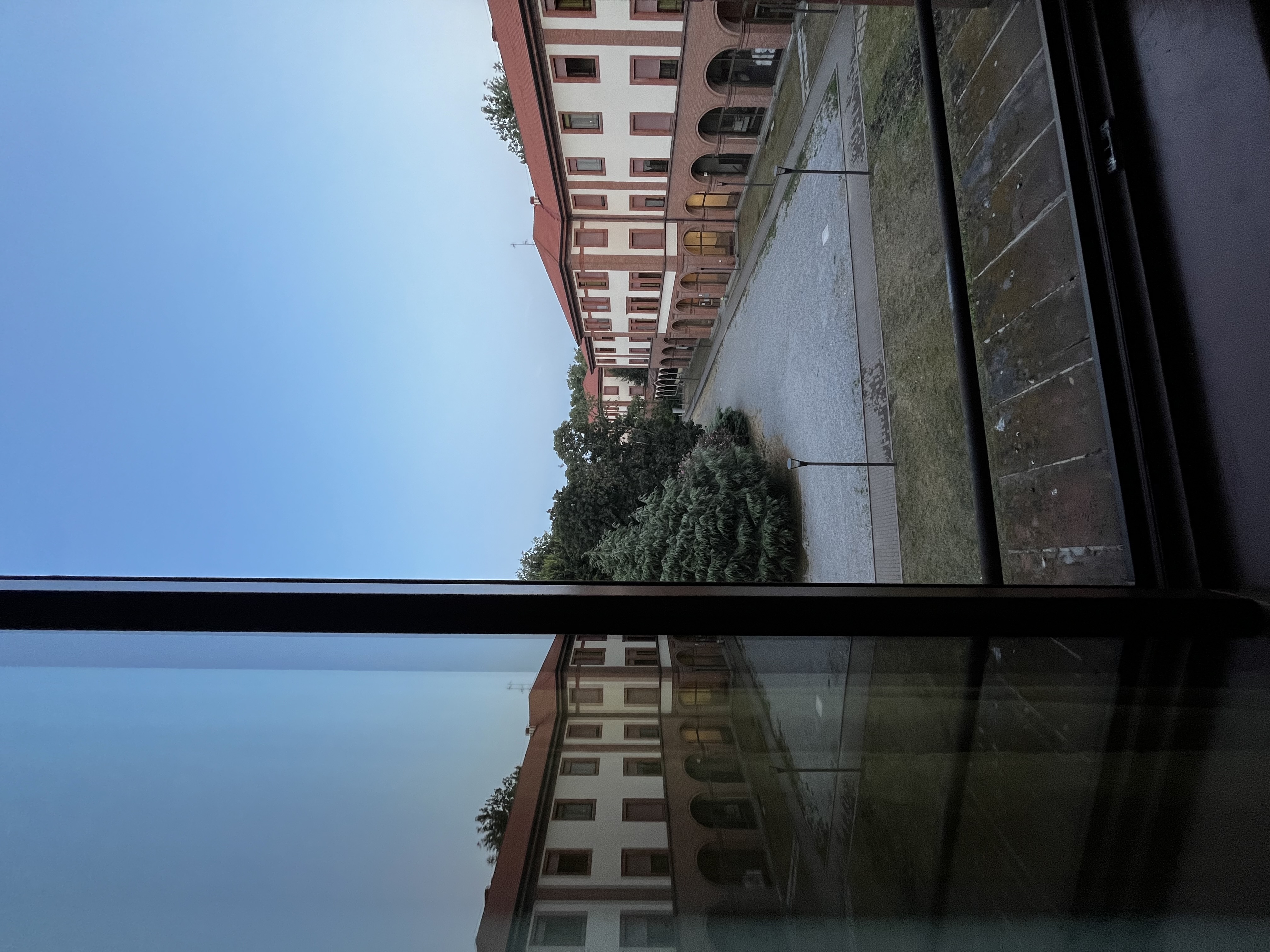 Innenhof mit Bäumen in Mailand, gespiegelt an Fensterscheibe